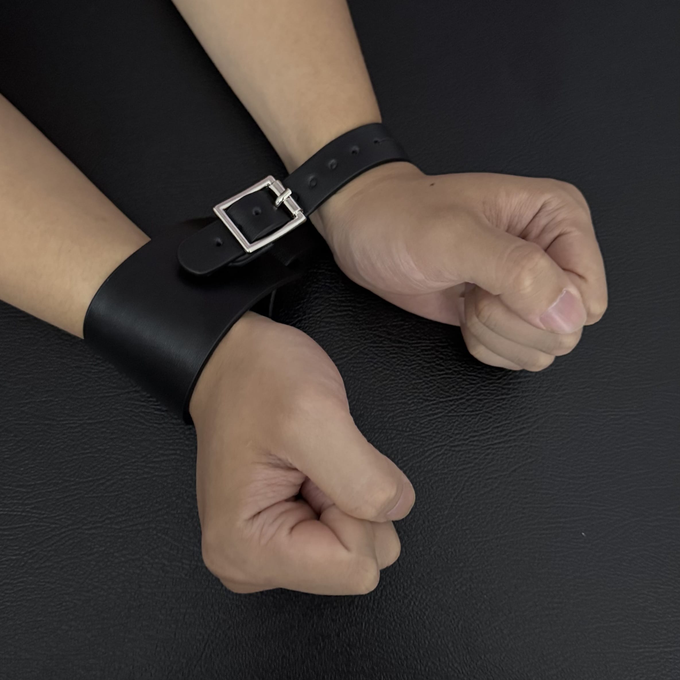 Black leather wrist cuffs with a buckle on a dark surface